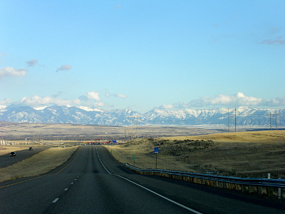 [View of rolling highway heading straight. In the distance are very tall snow-capped mountains.]